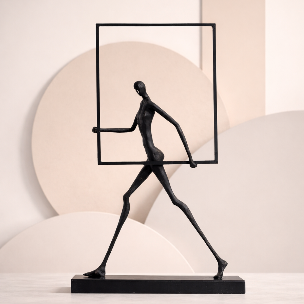 Black abstract sculpture of a figure holding a rectangular frame against a light background
